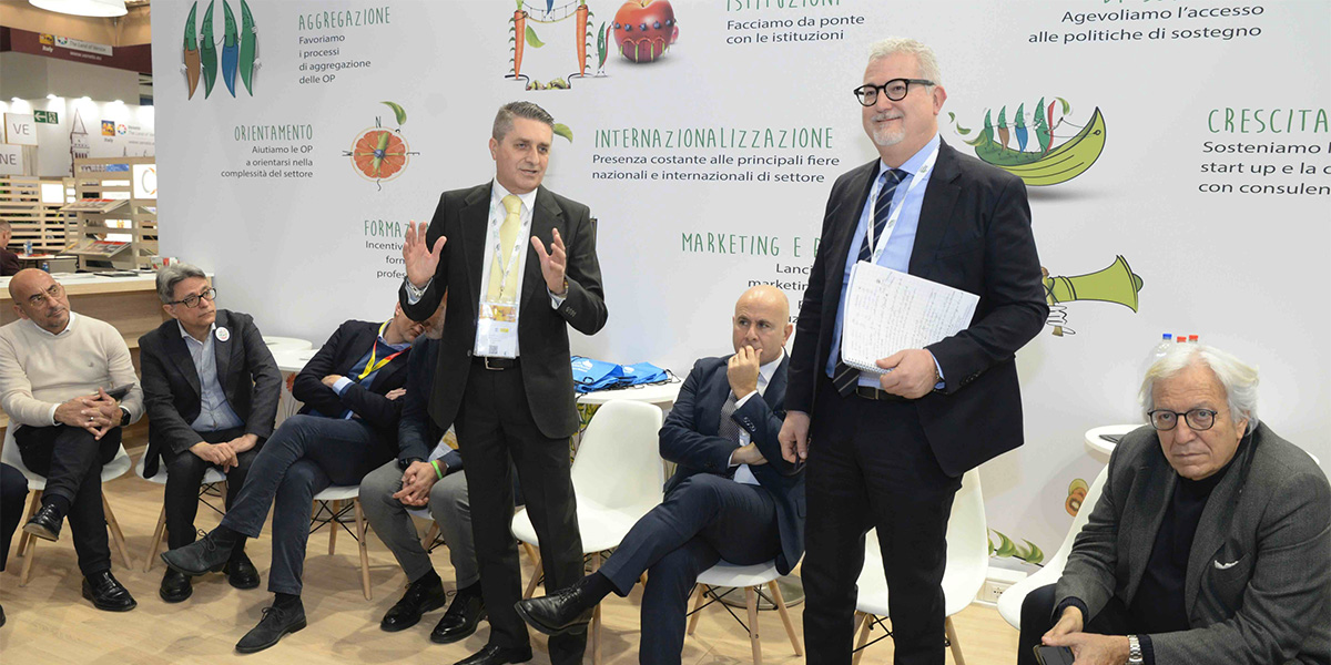 In piedi il presidente di Italia Ortofrutta Andrea Badursi e il direttore Vincenzo Falconi in una riunione a Fruit Logistica 2025. Al centro, seduto, l'europarlamentare Salvatore De Meo